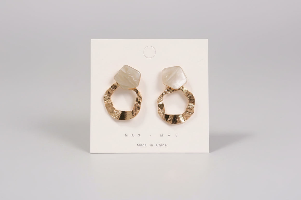 Pair of earrings on a display card held by a hand in a casual setting.