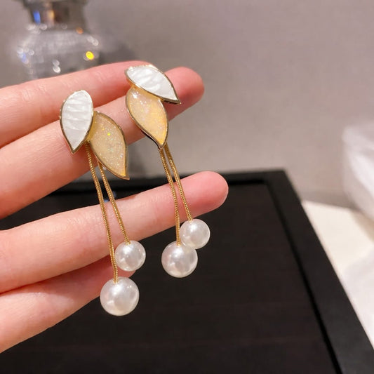 Pearl earrings with leaf-like designs held in a hand against a neutral background