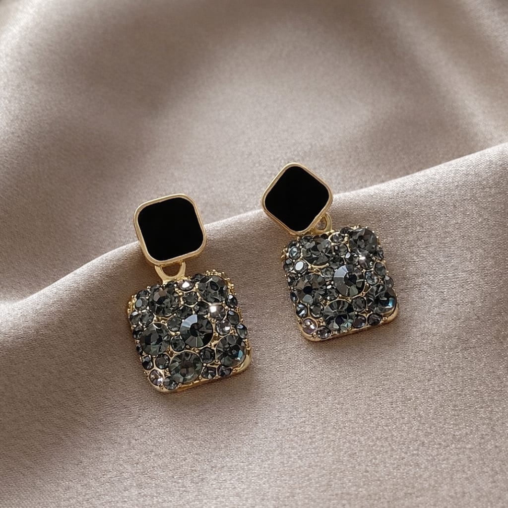 Pair of gold earrings with black and clear gemstones on a beige fabric background