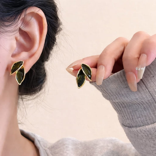 Close-up of a person wearing green leaf-shaped earrings with gold accents.