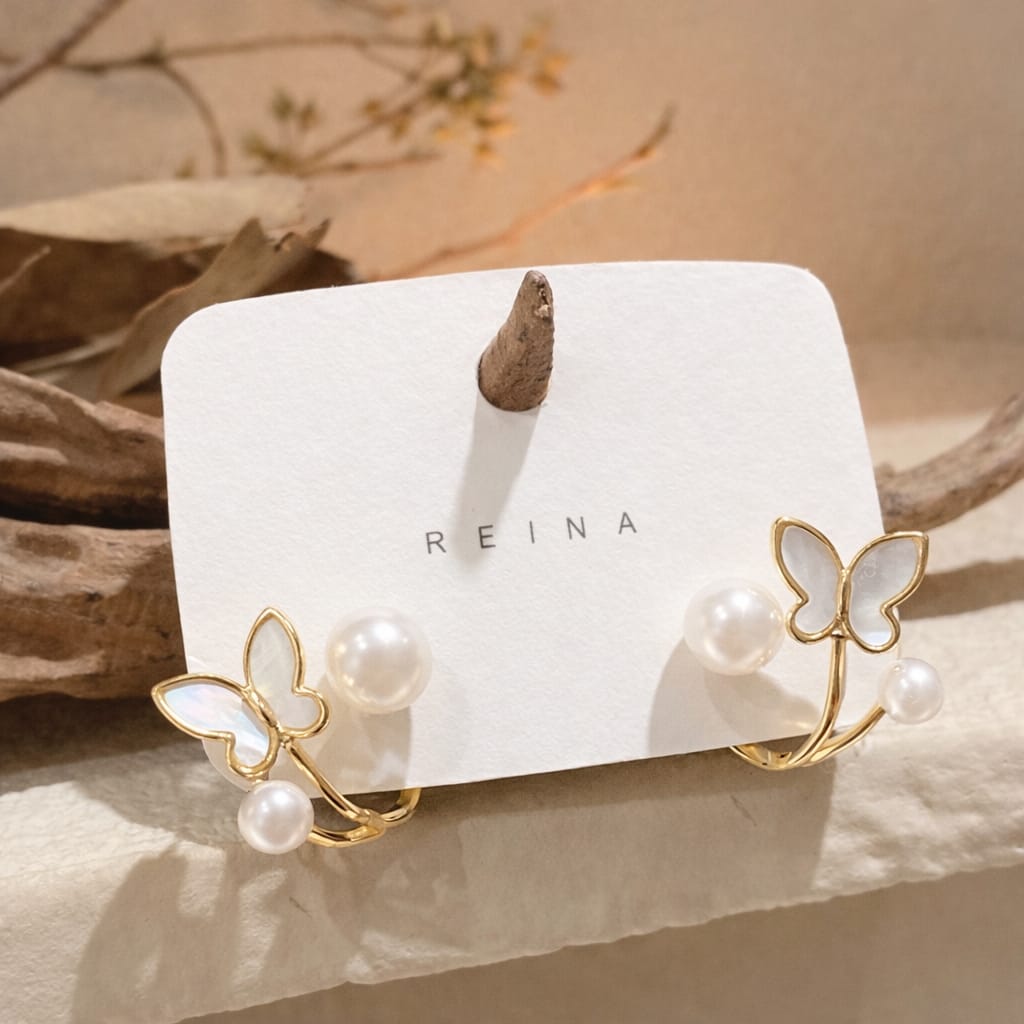Butterfly-shaped earrings with pearls on a Reina branded card.
